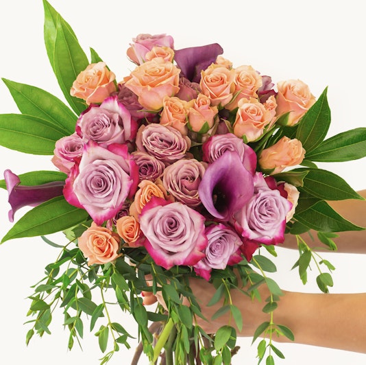 Vibrant bouquet featuring pink and purple roses with lush green leaves, elegantly held.
