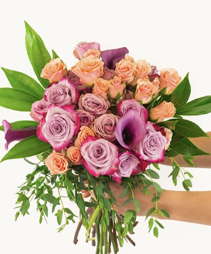Vibrant bouquet featuring pink and purple roses with lush green leaves, elegantly held.