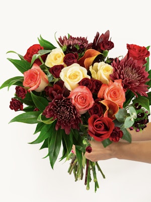 Vibrant bouquet featuring red, orange, and cream roses with lush greenery, perfect for celebrations.