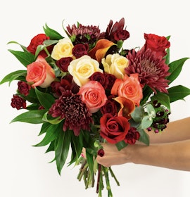 Vibrant bouquet featuring red, orange, and cream roses with lush greenery, perfect for celebrations.