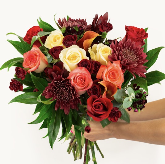 Vibrant bouquet featuring red, orange, and cream roses with lush greenery, perfect for celebrations.