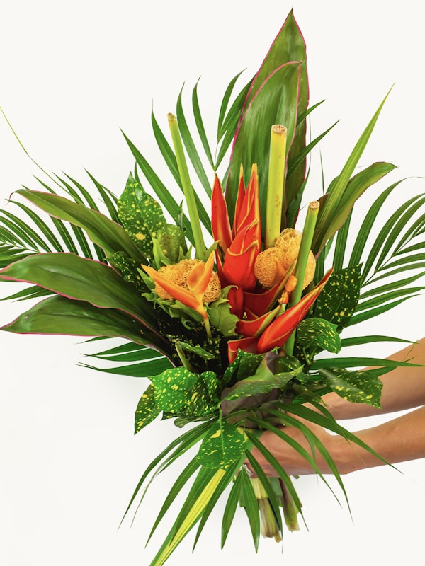 Vibrant tropical bouquet with oranges and greens, featuring heliconia, anthurium, and lush foliage against a clean white background.