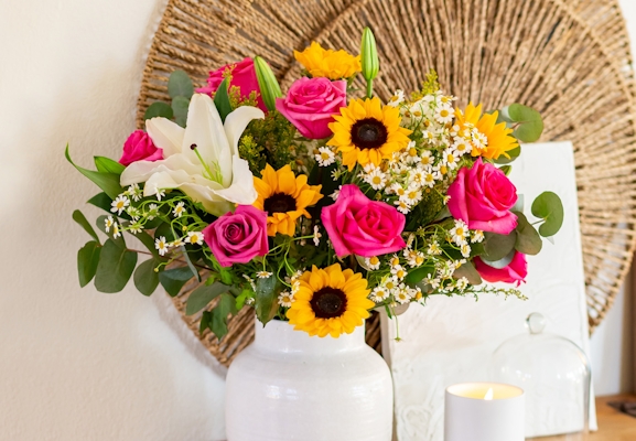 Bright floral arrangement featuring pink roses, sunflowers, and white lilies in a vase.