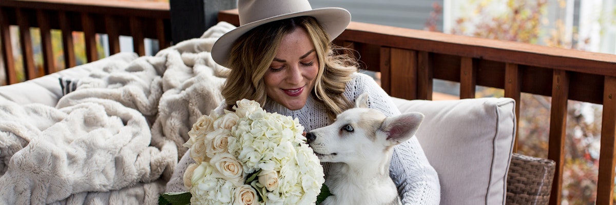 Woman holding a large bouquet of white roses while cuddling a cute dog on a cozy porch.
