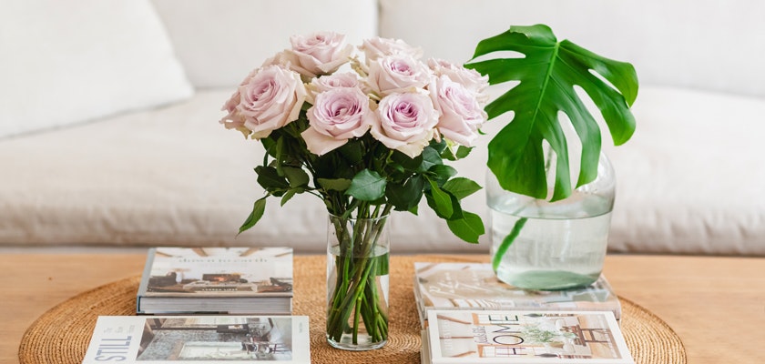 Elegant arrangement of pale pink roses in a glass vase, surrounded by decorative books and greenery.