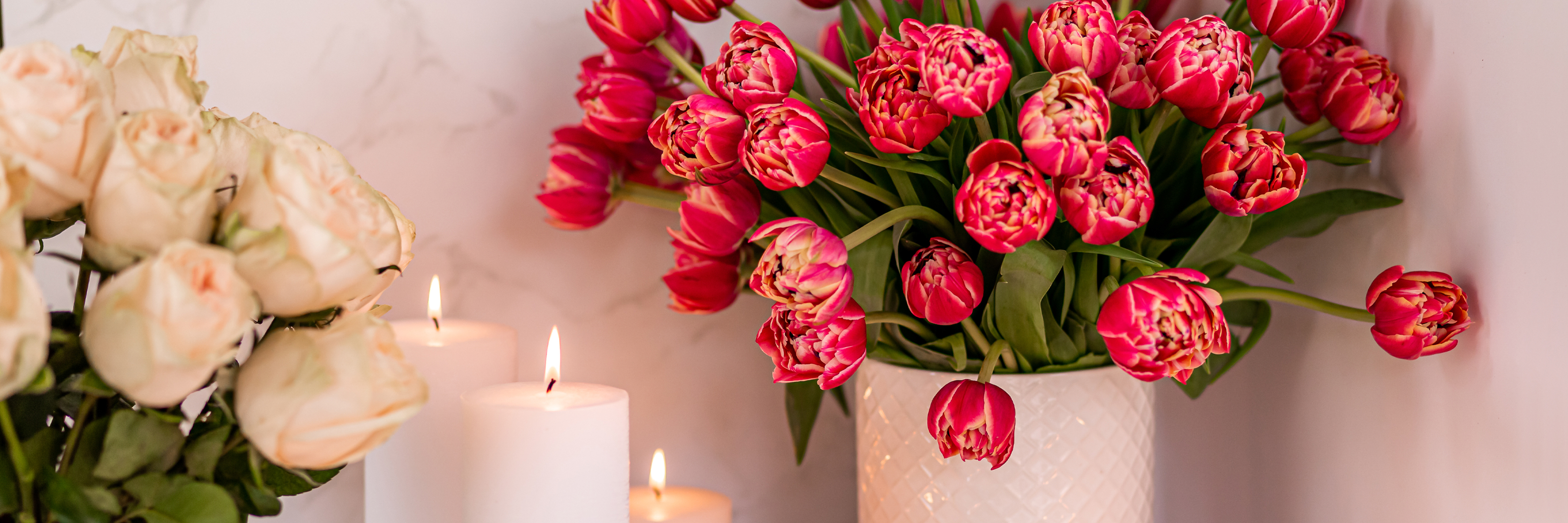 Vibrant pink tulips in a stylish vase, surrounded by soft candles and white roses.