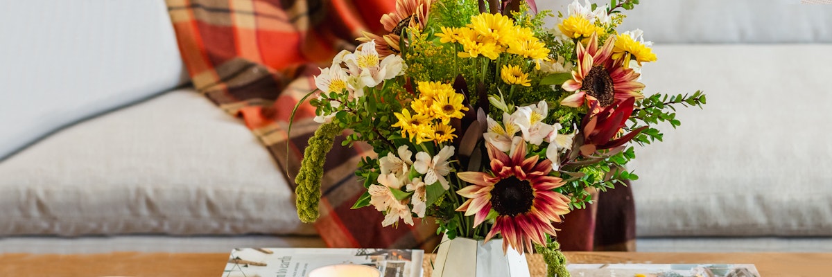 Bright floral arrangement featuring sunflowers, daisies, and greenery in a stylish vase.