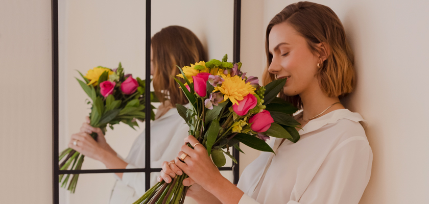 A woman in a white blouse holds a vibrant bouquet of pink and yellow flowers, radiating joy.