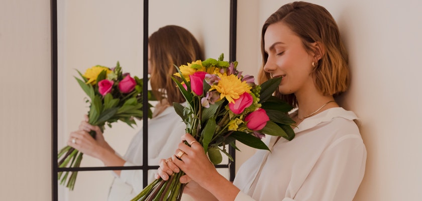 A woman in a white blouse holds a vibrant bouquet of pink and yellow flowers, radiating joy.