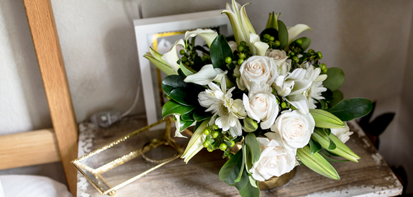 Elegant floral arrangement featuring white roses, lilies, and greenery in a chic gold vase.