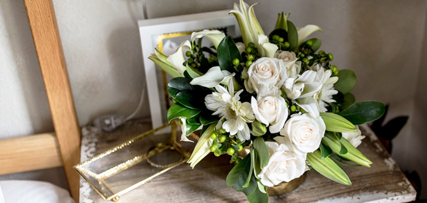 Elegant floral arrangement featuring white roses, lilies, and greenery in a chic gold vase.
