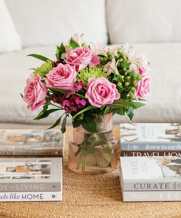 Elegant floral arrangement featuring pink roses and white lilies in a glass vase on a coffee table with assorted lifestyle magazines.