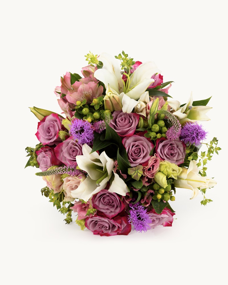 A vibrant bouquet of mixed flowers featuring pink roses, white lilies, and purple accents with green foliage against a white background.
