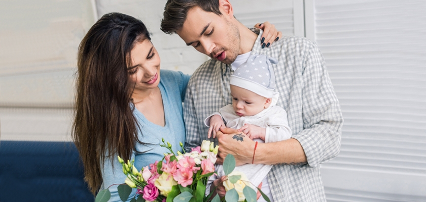 A joyful couple holding a vibrant floral bouquet while adoring their newborn baby.