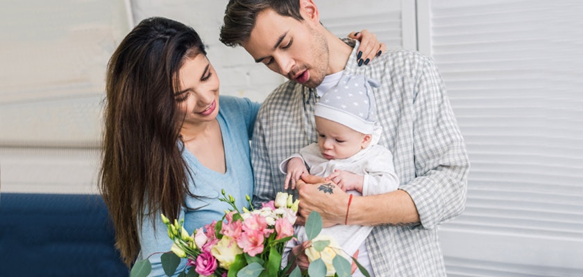 A joyful couple holding a vibrant floral bouquet while adoring their newborn baby.
