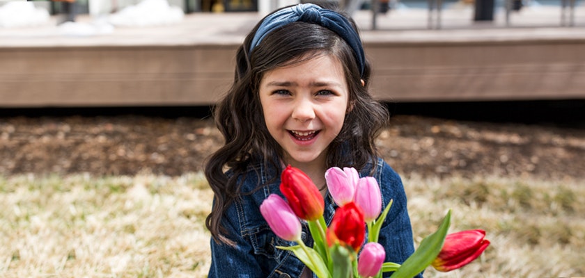 A cheerful girl in a denim jacket holds a vibrant bouquet of tulips in pink and red.