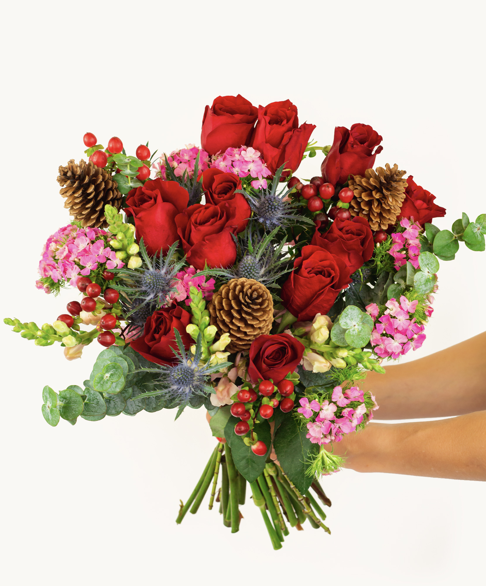 Vibrant bouquet featuring red roses, pink blooms, and natural accents like pine cones.