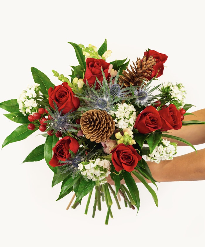 Vibrant bouquet featuring red roses, pinecones, and delicate white flowers, beautifully arranged.