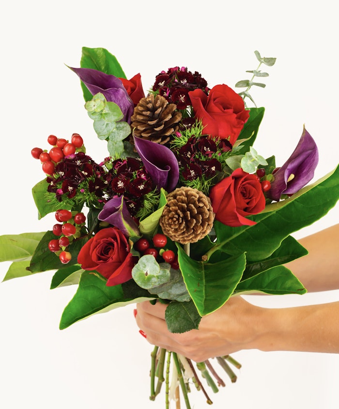 Vibrant bouquet featuring red roses, pinecones, and green foliage, perfect for winter.