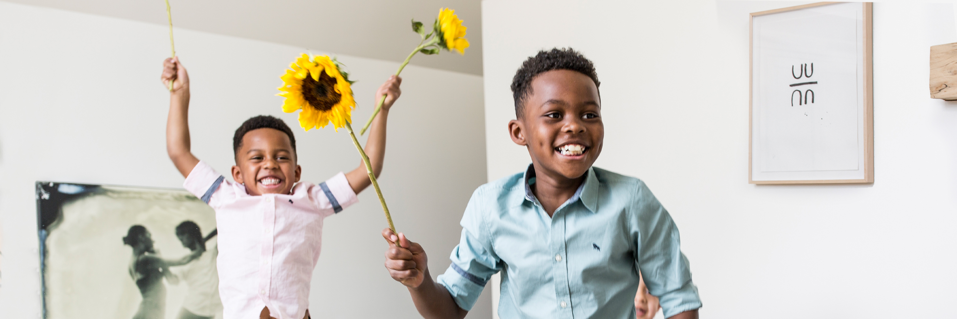 Two joyful boys playing inside, holding bright sunflowers, exuding happiness and energy.