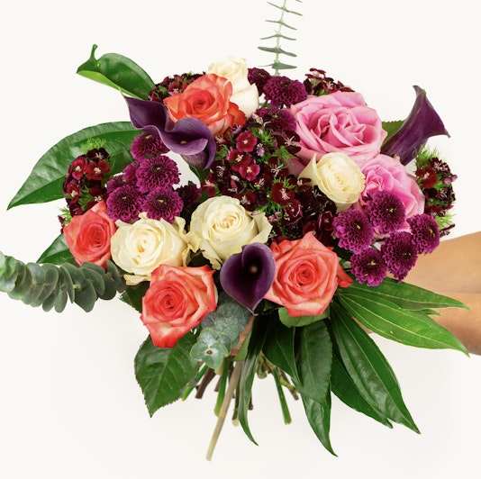 Vibrant floral bouquet featuring pink roses, purple calla lilies, and lush greenery.