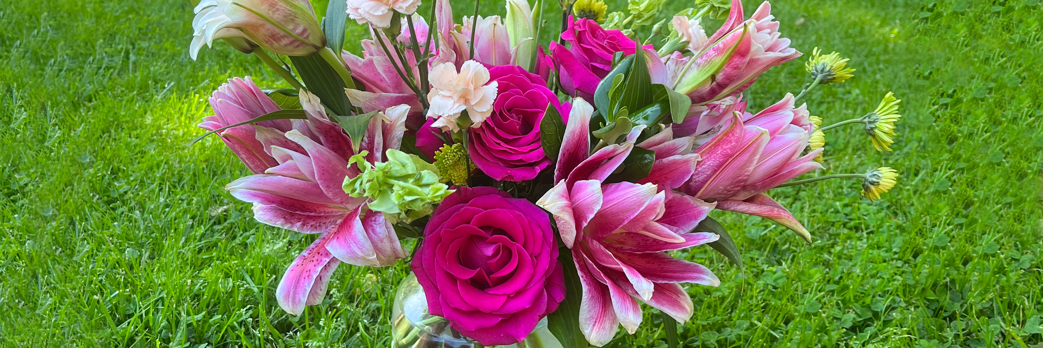 Vivid floral arrangement featuring pink lilies, roses, and green accents in a lush garden setting.
