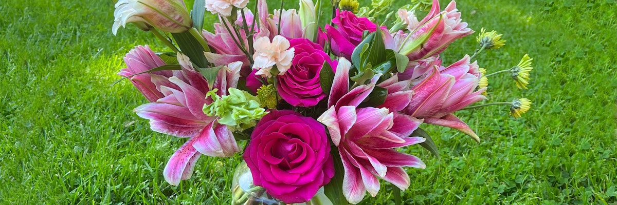 Vivid floral arrangement featuring pink lilies, roses, and green accents in a lush garden setting.