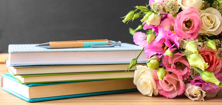 A stack of colorful books beside a vibrant bouquet of pink and white flowers.