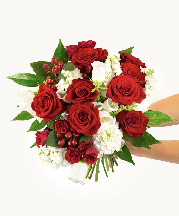 Vibrant bouquet of red roses and white flowers with green foliage and red berries against a light background, ideal for romantic occasions or as a gift.