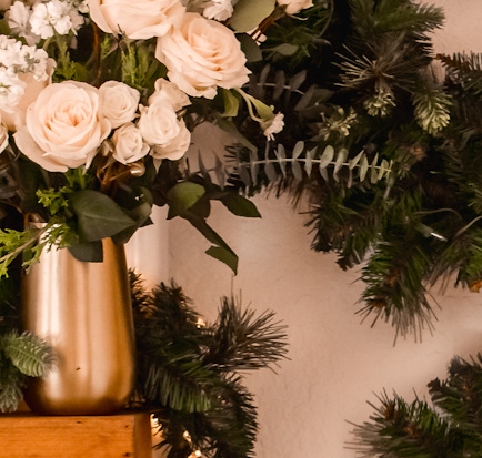 Elegant cream roses and delicate white flowers in a chic gold vase, surrounded by lush greenery.