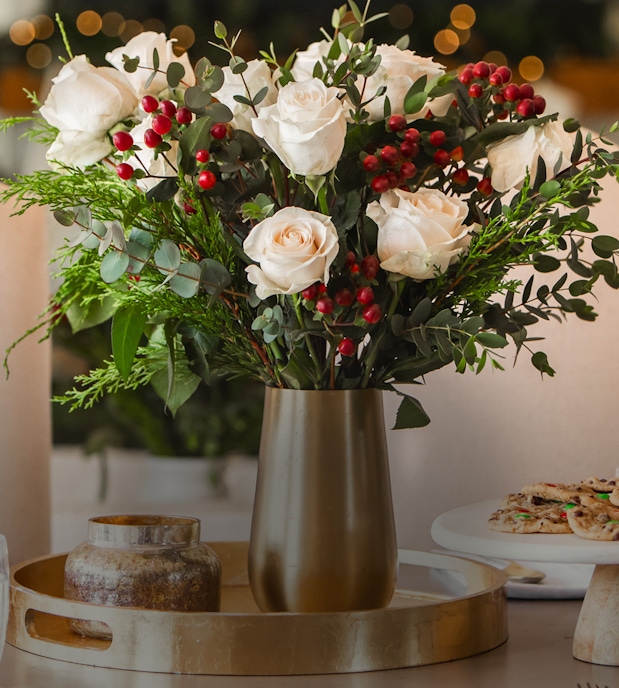 Elegant white roses and lush greenery in a stylish gold vase, perfect for festive decor.