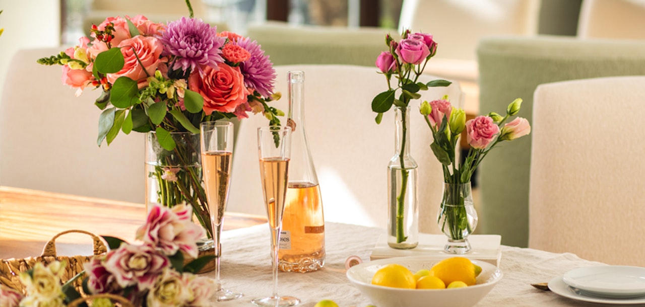 Elegant table setting featuring a colorful bouquet of flowers, champagne flutes, a bottle of rose, and a bowl of lemons, showcasing a warm, inviting dining atmosphere.