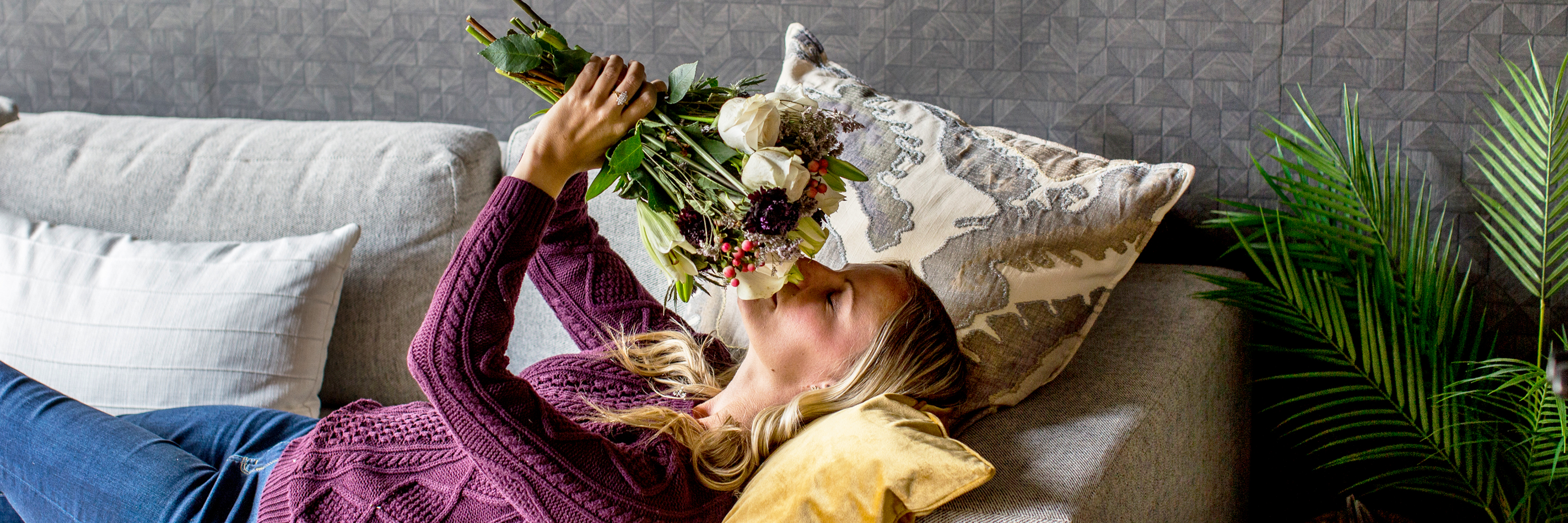 A woman relaxes on a couch, admiring a fresh bouquet of colorful flowers.