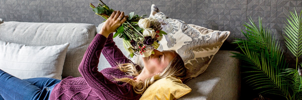 A woman relaxes on a couch, admiring a fresh bouquet of colorful flowers.