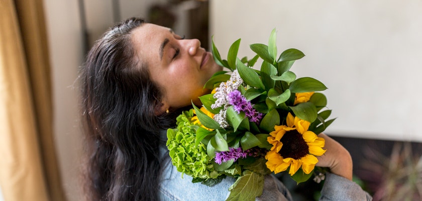 A woman happily embraces a vibrant bouquet of sunflowers and assorted flowers.