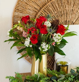 Vibrant red roses adorned with white flowers and greenery in a stylish vase.