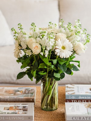 Elegant white floral bouquet featuring roses and gerbera daisies in a stylish glass vase.