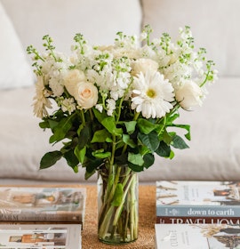 Elegant white floral bouquet featuring roses and gerbera daisies in a stylish glass vase.
