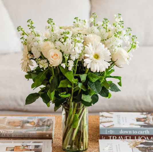 Elegant white floral bouquet featuring roses and gerbera daisies in a stylish glass vase.