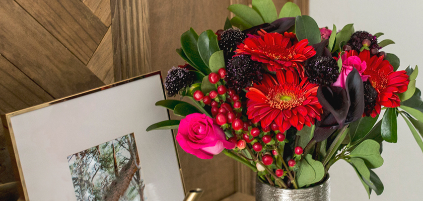 Vibrant floral arrangement featuring red gerbera daisies, pink roses, and lush greenery.