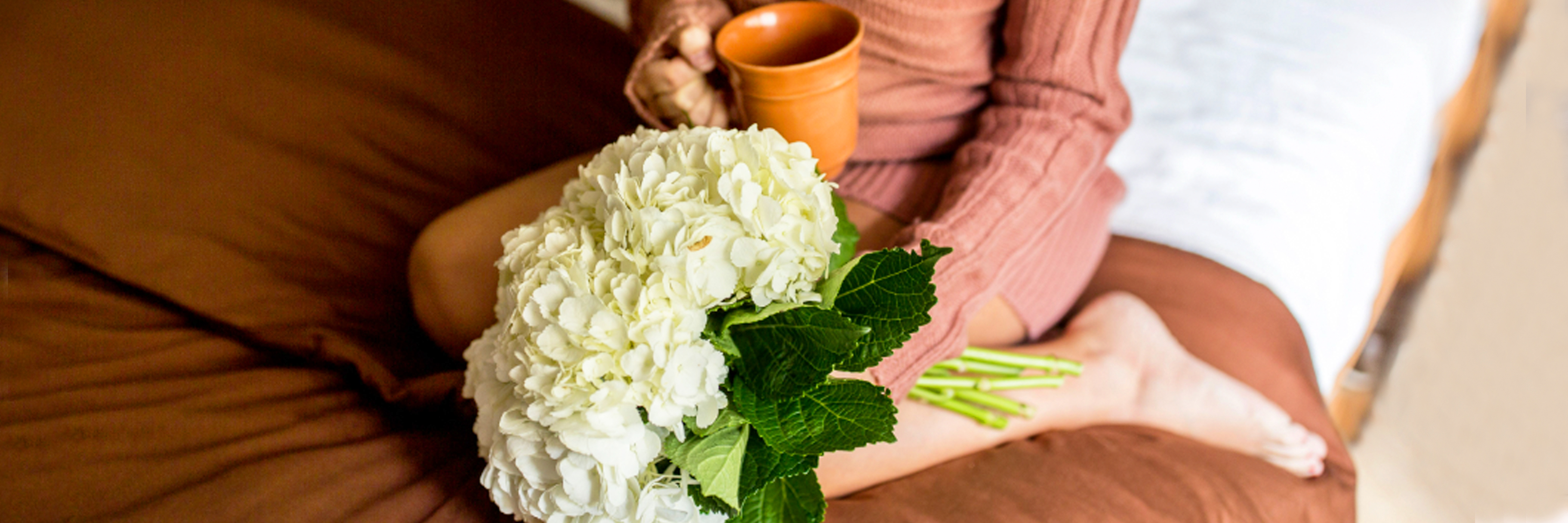 Cozy morning scene featuring a woman holding a lush white hydrangea bouquet while sipping tea.