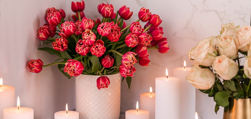 Vibrant pink tulips arranged in a white vase, surrounded by lit candles for a cozy ambiance.