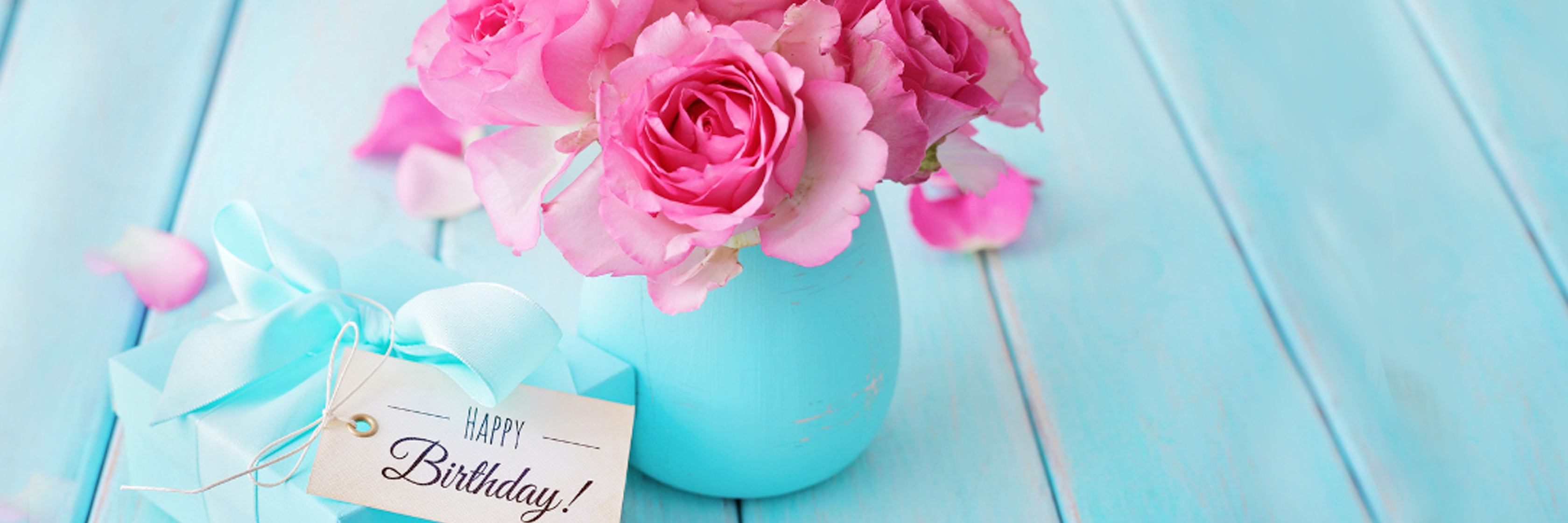 Delicate pink roses in a turquoise vase beside a birthday gift, perfect for celebrations.