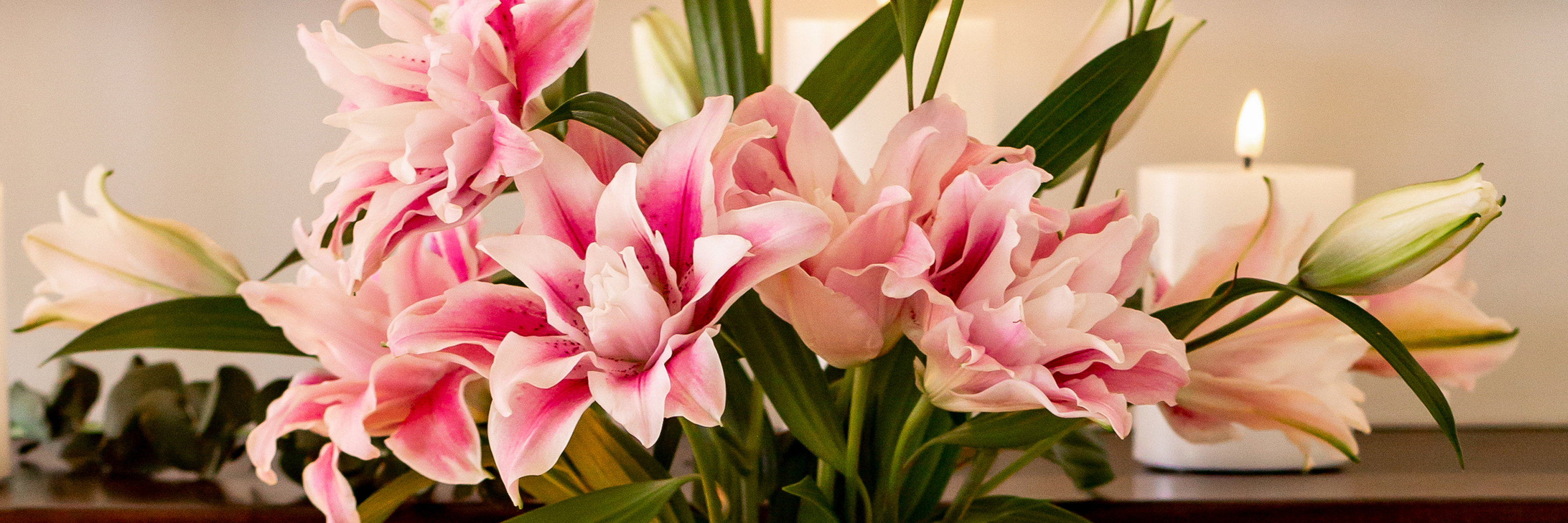 Beautiful pink lilies arranged elegantly with green leaves and candles, perfect for decoration.