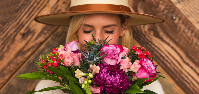 A woman in a wide-brimmed hat holds a vibrant floral bouquet, enjoying its fragrance.