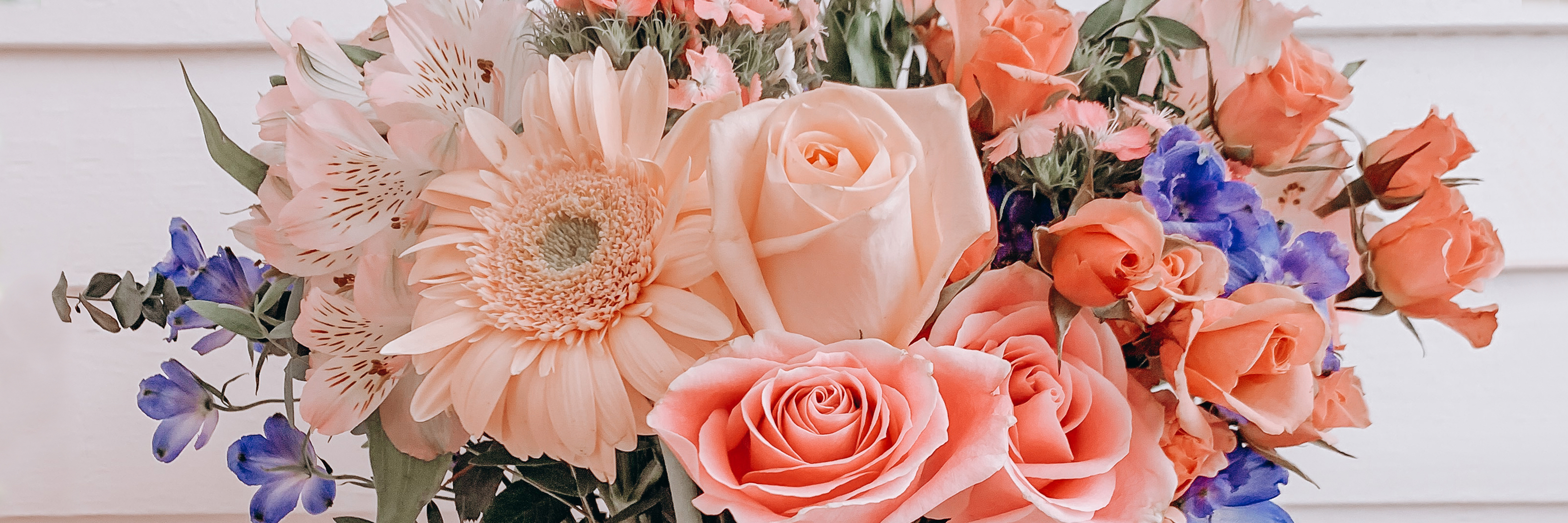 A vibrant floral arrangement featuring pink and blue roses, gerbera daisies, and lush greenery.