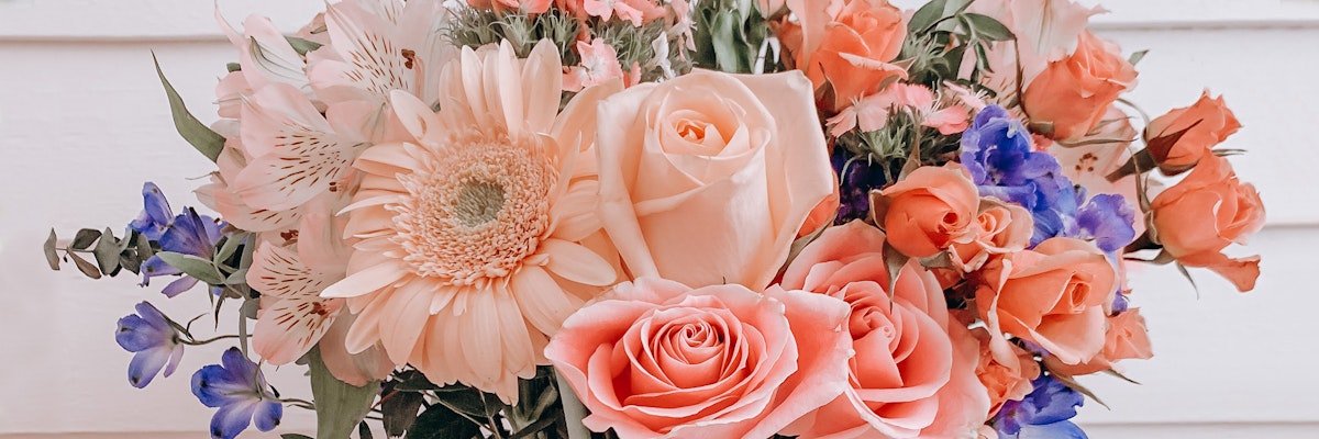 A vibrant floral arrangement featuring pink and blue roses, gerbera daisies, and lush greenery.