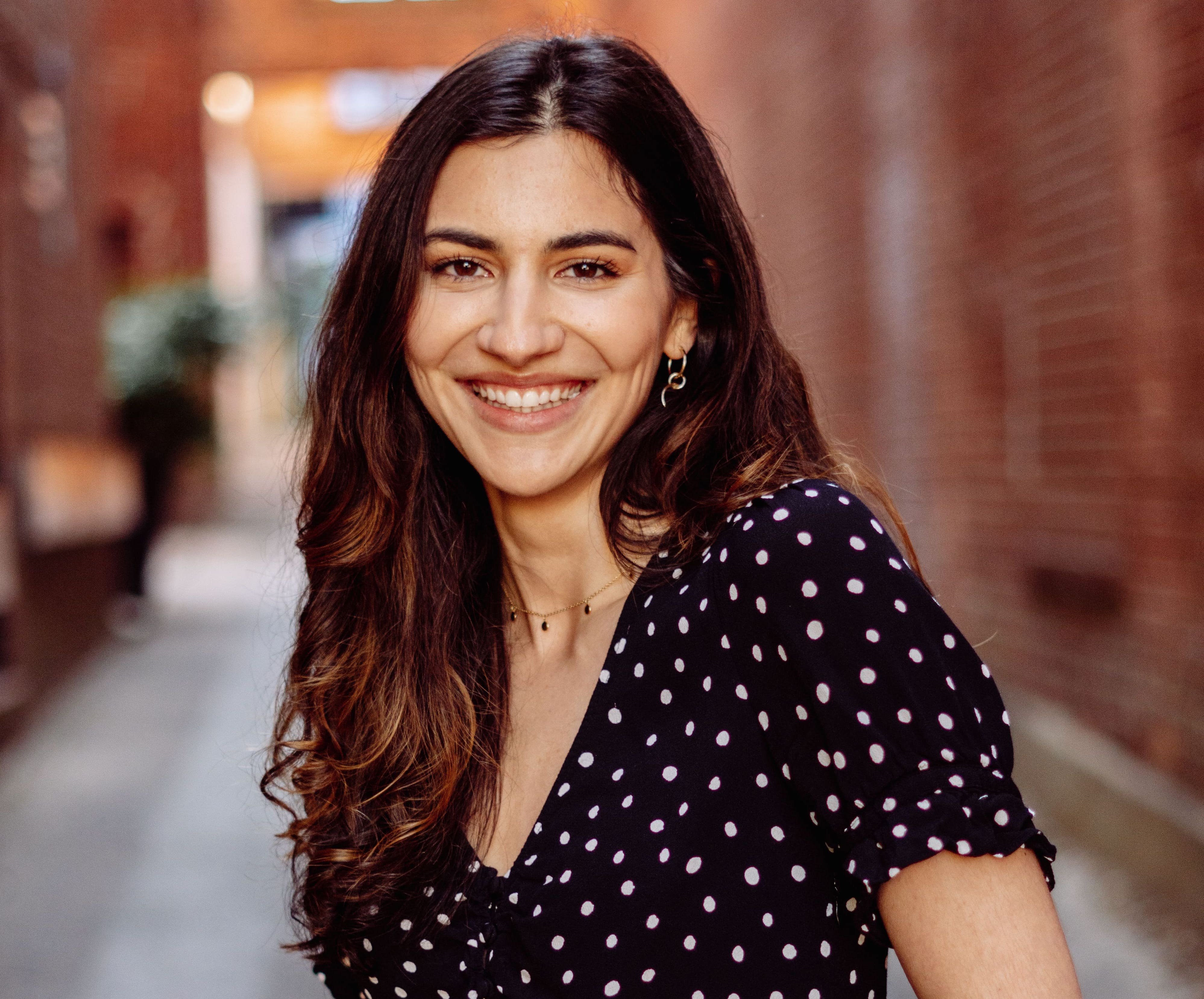 Smiling woman in a polka dot dress, posing in a charming urban alleyway.