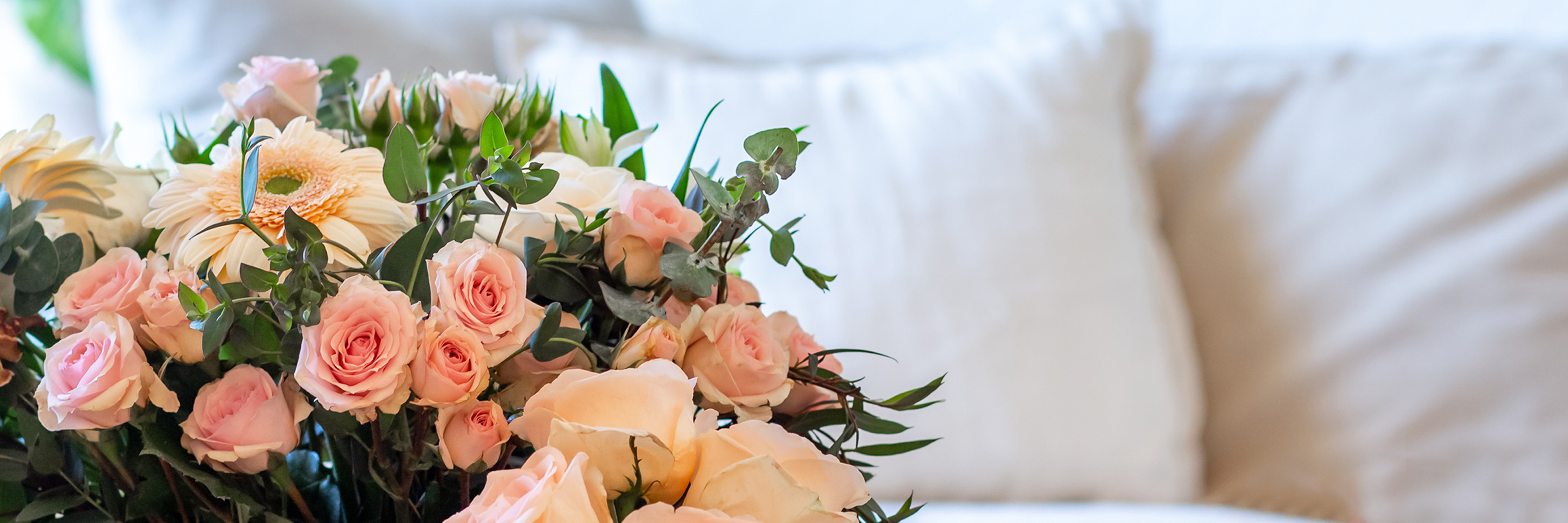Elegant floral arrangement featuring soft pink roses and white gerbera daisies on a cozy couch.