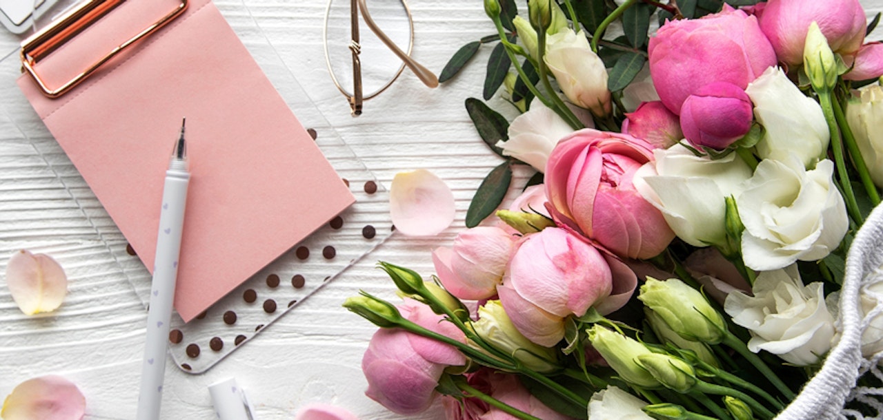 A vibrant arrangement of pink and white flowers alongside a stylish notebook and pen.